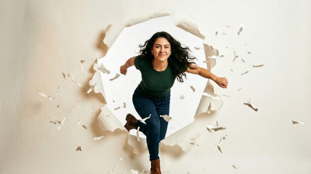 Konceptuálna fotografia. Mladá žena sebavedomo prelamuje papierovú stenu, teplé štúdiové osvetlenie, odhodlaný výraz s jemným úsmevom. Čisté biele pozadie s vznášajúcimi sa útržkami roztrhaného papiera. Nálada je posilňujúca, búrajúca mýty a odvážna. Žiadny text, žiadne logá. Hlavička redakčného blogu. Pomer strán 16:9.